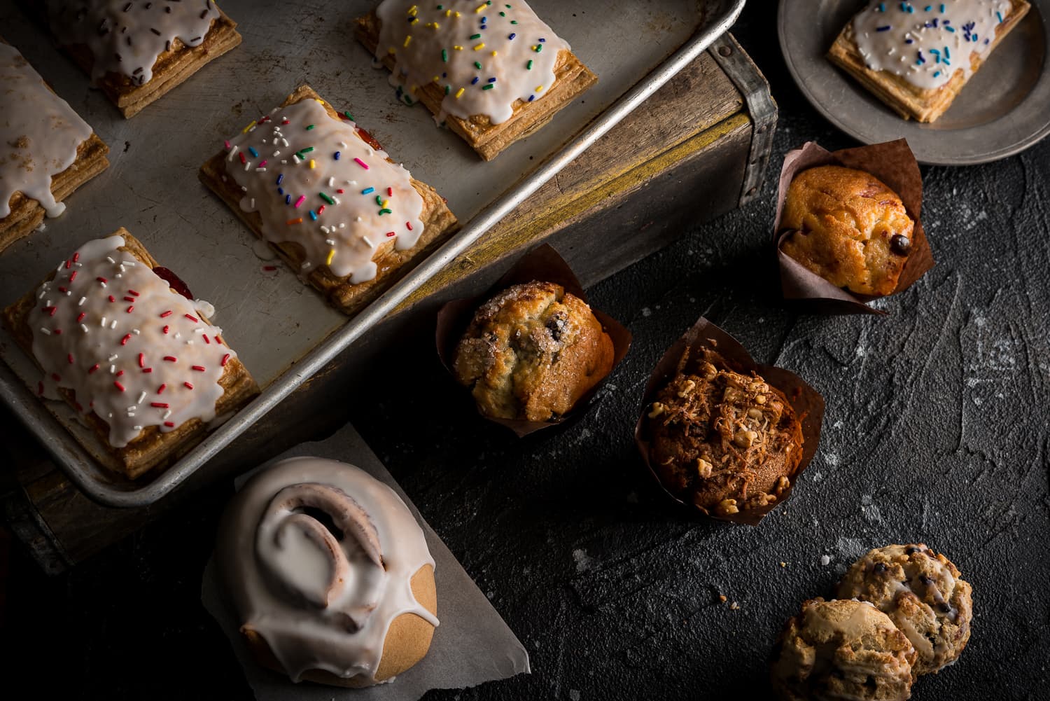 A sheet pan of frosted hand pies, muffins and a cinnamon roll