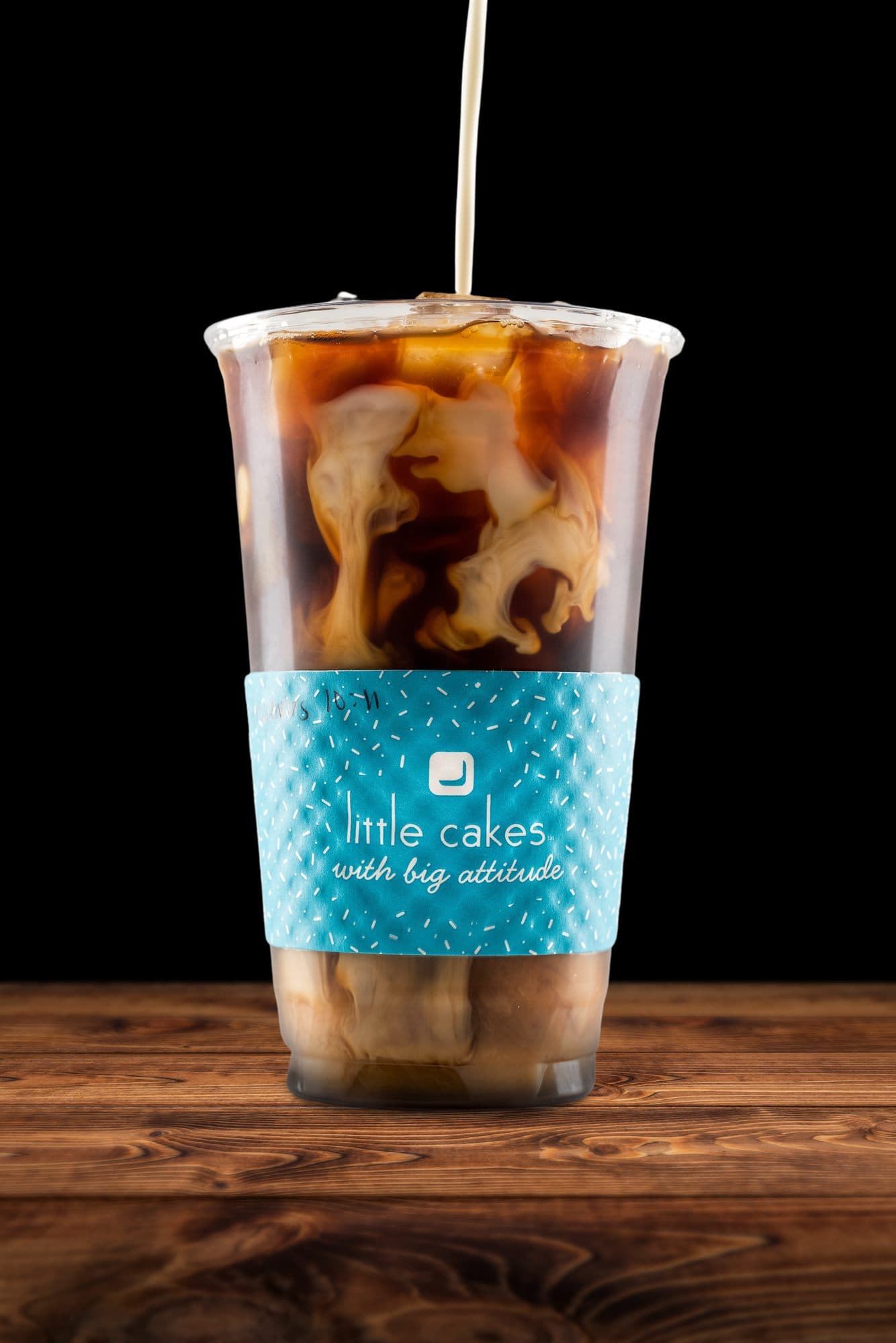 Iced latte with cream swirling in, in a branded teal Little Cakes sleeve, coffee in Alexandria and Pineville LA