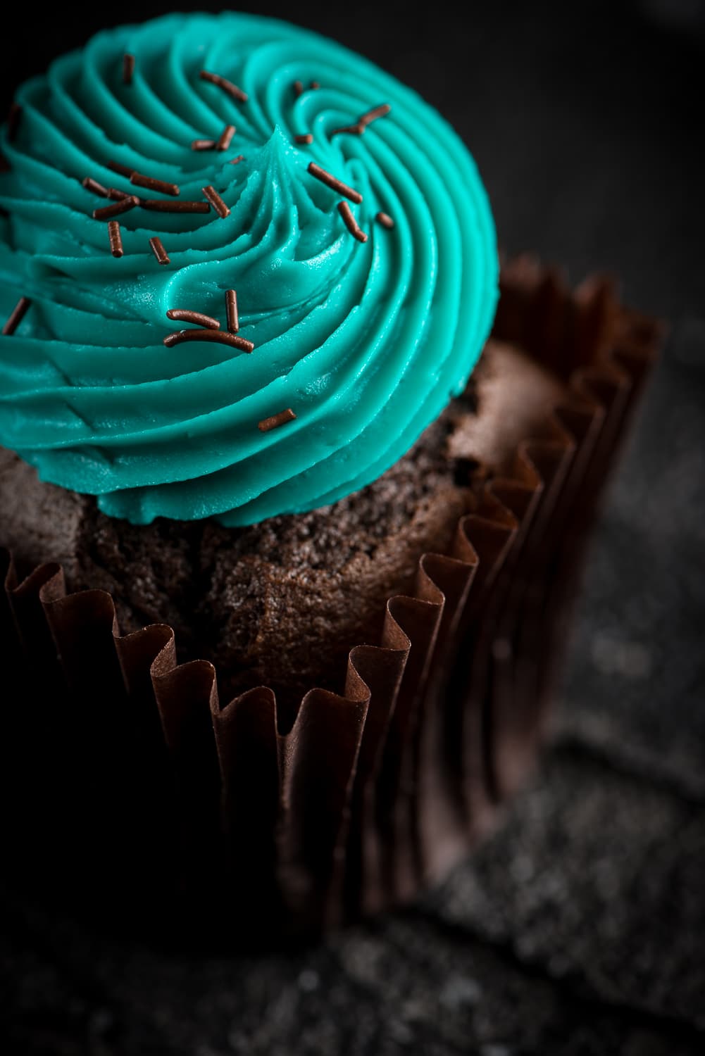 A chocolate cupcake with the signature teal buttercream swirl